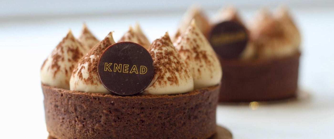Chocolate tart with cream and a 'KNEAD' logo on a blurred background. Award winning tiramisu. 